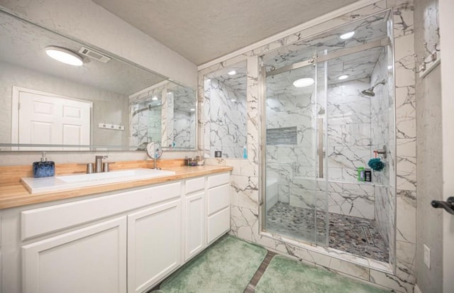 bathroom with a marble finish shower, visible vents, and vanity