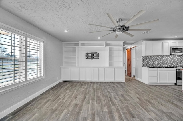 unfurnished living room with a textured ceiling, baseboards, light wood-style flooring, and a ceiling fan