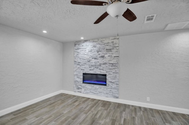 unfurnished living room with visible vents, a textured wall, a stone fireplace, a textured ceiling, and wood finished floors