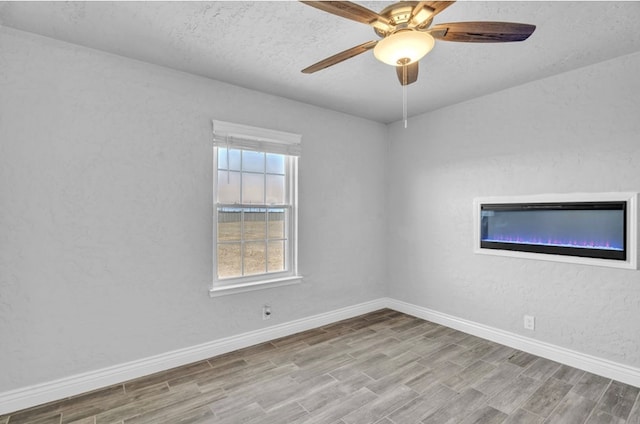 empty room with a textured wall, light wood finished floors, and baseboards