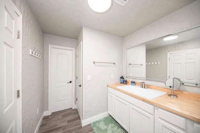 bathroom with a textured wall, wood finished floors, vanity, visible vents, and baseboards