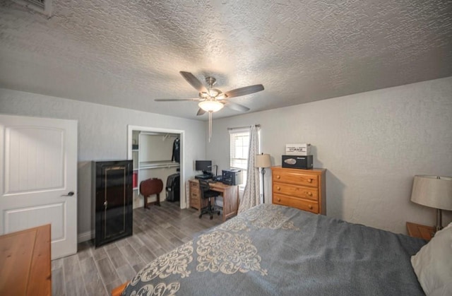 bedroom with a textured wall, wood finish floors, visible vents, a ceiling fan, and a closet