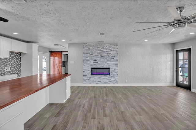 unfurnished living room with wood finished floors, ceiling fan, a textured ceiling, and a barn door