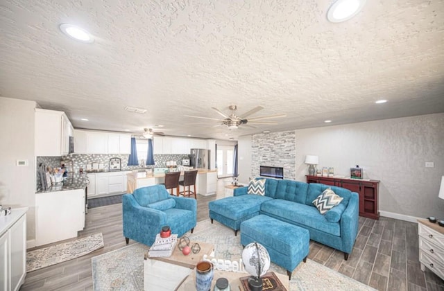 living room featuring ceiling fan, a textured ceiling, a fireplace, and wood tiled floor