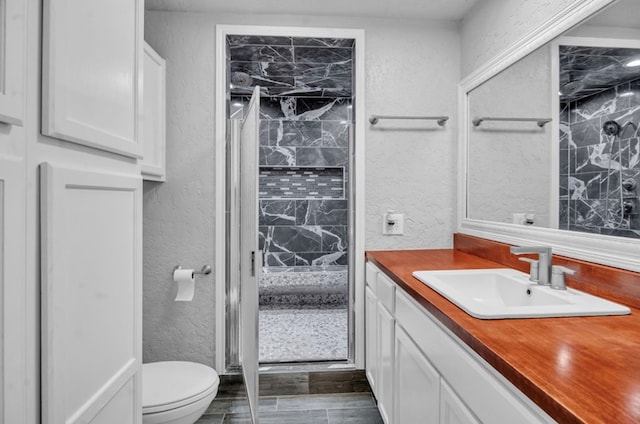 full bathroom featuring toilet, a stall shower, vanity, and a textured wall