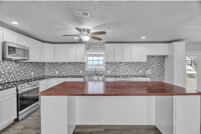 kitchen featuring wall oven, stainless steel microwave, white cabinetry, wooden counters, and a sink