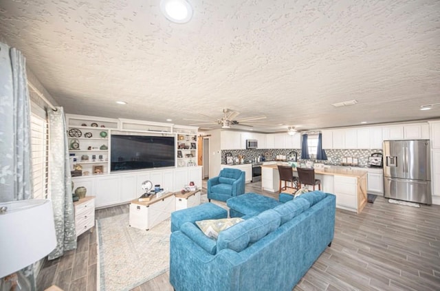 living area featuring a textured ceiling, wood finish floors, a ceiling fan, and recessed lighting