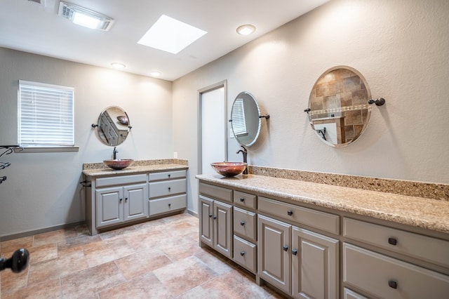 bathroom with a skylight, baseboards, visible vents, a sink, and two vanities