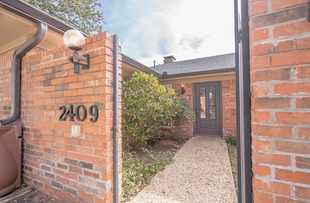 doorway to property with brick siding and roof with shingles