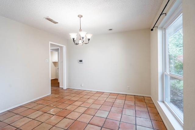 empty room with a notable chandelier, a textured ceiling, baseboards, and light tile patterned floors