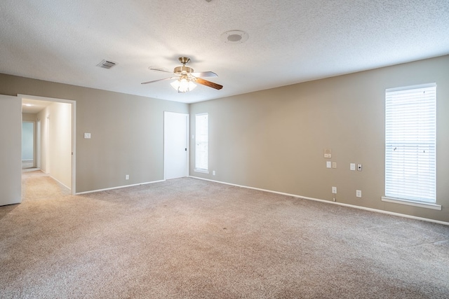 spare room with light colored carpet, visible vents, ceiling fan, a textured ceiling, and baseboards