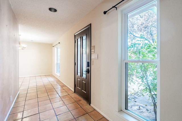 entryway with a textured ceiling, light tile patterned flooring, a chandelier, and baseboards