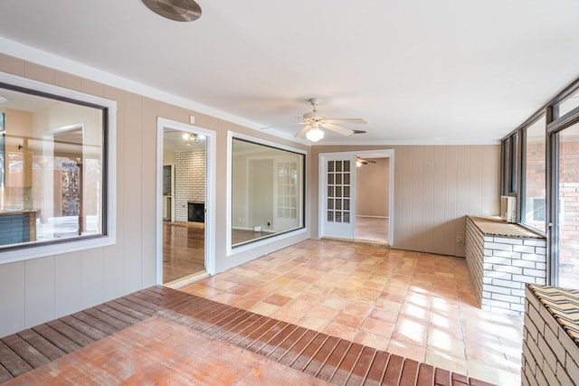 unfurnished sunroom with a brick fireplace and ceiling fan