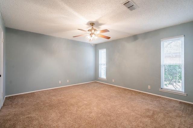 carpeted empty room with ceiling fan, a textured ceiling, visible vents, and a wealth of natural light