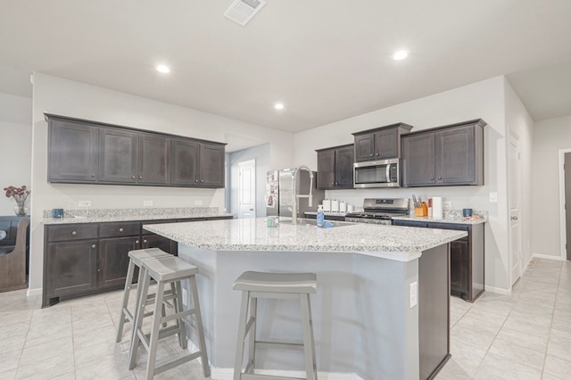 kitchen featuring stainless steel appliances, a kitchen bar, a center island with sink, and visible vents