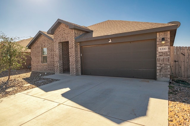 view of front of house featuring a garage, brick siding, a shingled roof, fence, and driveway