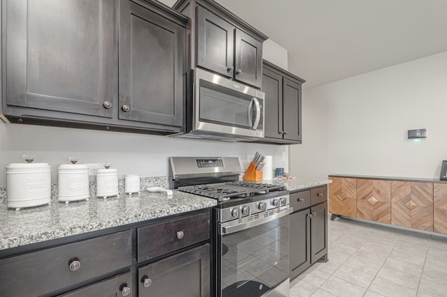 kitchen with light tile patterned floors, light stone counters, stainless steel appliances, and dark brown cabinets