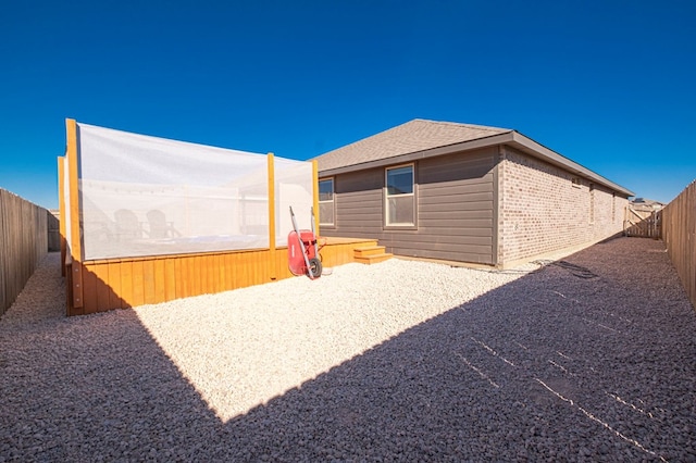 exterior space with a patio area, a fenced backyard, roof with shingles, and brick siding