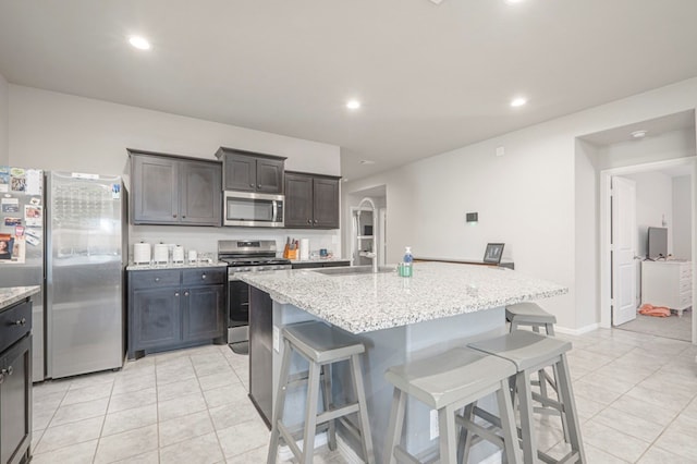 kitchen with stainless steel appliances, dark brown cabinets, a kitchen bar, and a center island with sink