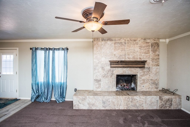 unfurnished living room with a textured ceiling, carpet floors, ornamental molding, and a tiled fireplace