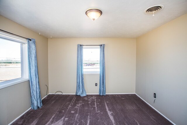 empty room featuring a healthy amount of sunlight and dark colored carpet