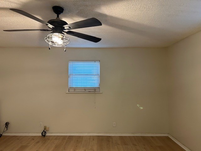 empty room featuring light wood finished floors, baseboards, a textured ceiling, and ceiling fan