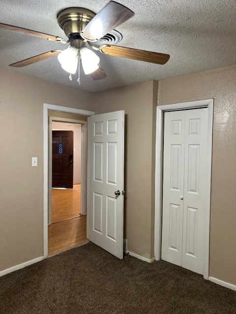 unfurnished bedroom with ceiling fan, baseboards, a closet, a textured ceiling, and dark colored carpet