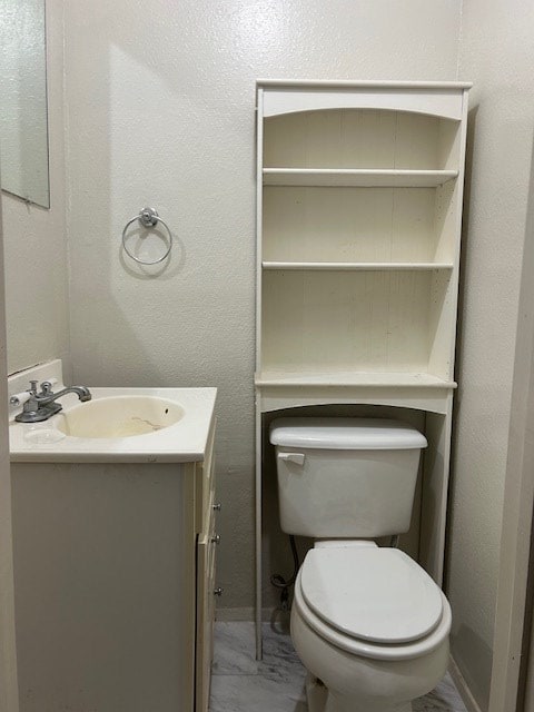 half bath with toilet, marble finish floor, vanity, and a textured wall
