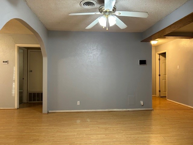 unfurnished room with light wood finished floors, visible vents, and arched walkways