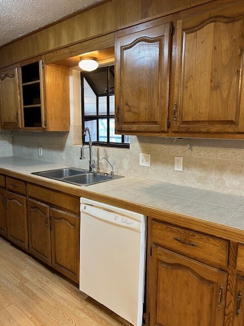 kitchen featuring tile countertops, light wood-type flooring, white dishwasher, a textured ceiling, and a sink