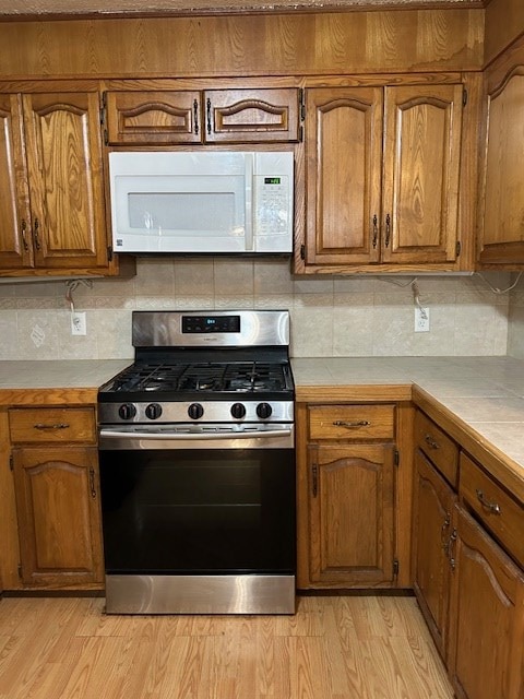 kitchen featuring tile countertops, stainless steel gas stove, white microwave, and brown cabinetry