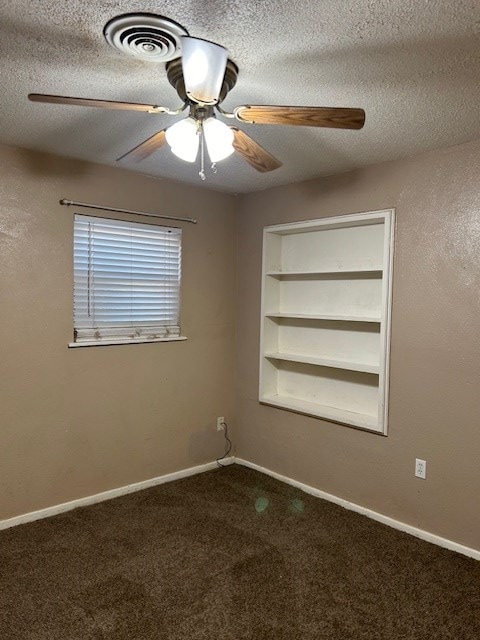 spare room with built in features, a textured ceiling, baseboards, and dark colored carpet