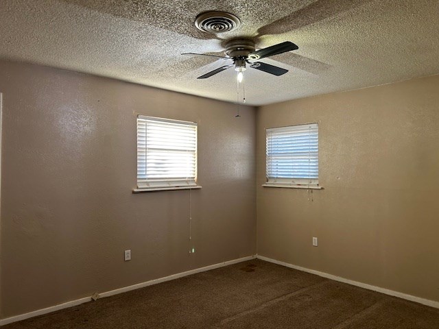 carpeted empty room with visible vents, baseboards, a textured ceiling, and ceiling fan