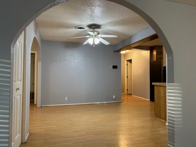 empty room with arched walkways, wood finished floors, visible vents, and ceiling fan