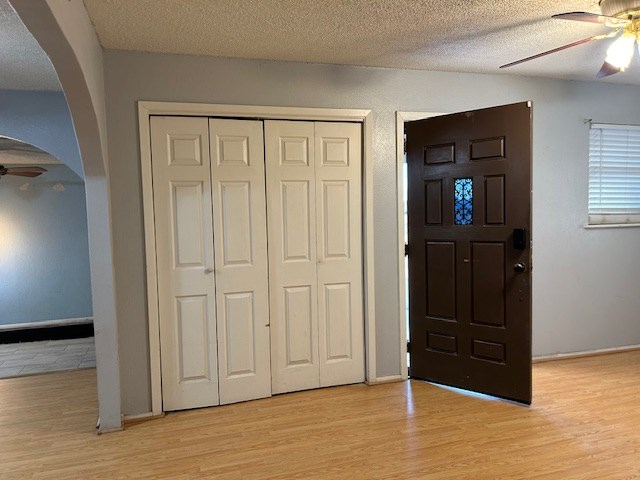 foyer with a textured ceiling, light wood-style flooring, arched walkways, and ceiling fan