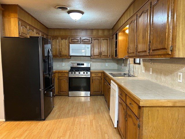 kitchen with visible vents, brown cabinets, light wood-style flooring, a sink, and white appliances