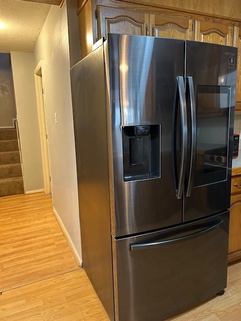 kitchen featuring baseboards, light wood-style floors, brown cabinetry, stainless steel fridge, and a textured ceiling