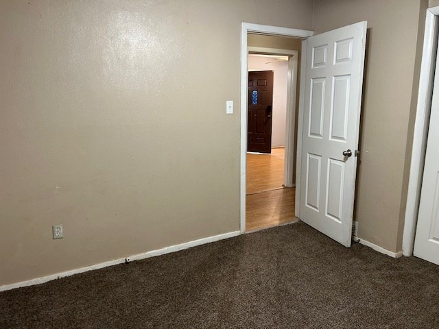 unfurnished room featuring baseboards and dark carpet