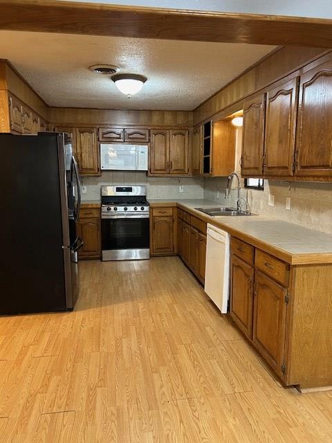kitchen featuring light wood-style flooring, a sink, appliances with stainless steel finishes, a textured ceiling, and brown cabinets