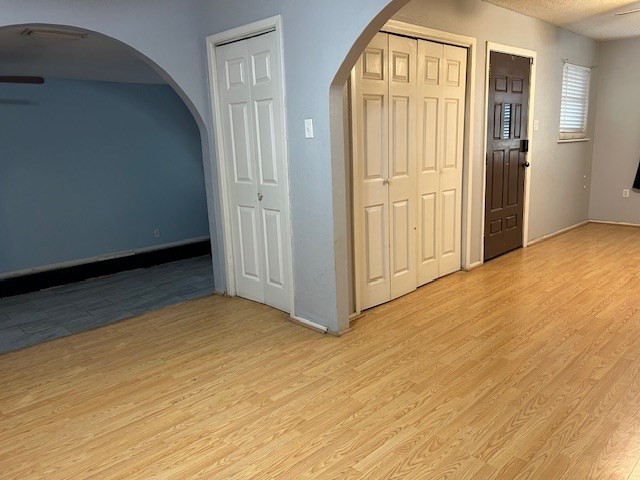 entrance foyer with arched walkways, a textured ceiling, and light wood finished floors
