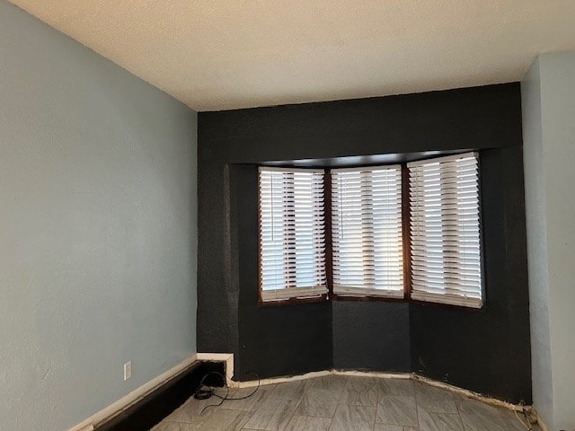 unfurnished room with baseboards and a textured ceiling