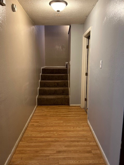 hallway with light wood-type flooring, a textured ceiling, stairway, baseboards, and a textured wall