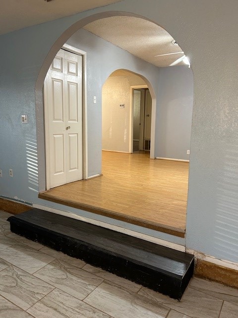 hallway featuring wood finished floors, a textured wall, and arched walkways