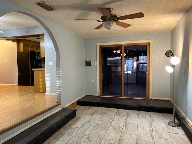 interior space featuring visible vents, a textured ceiling, arched walkways, baseboards, and ceiling fan
