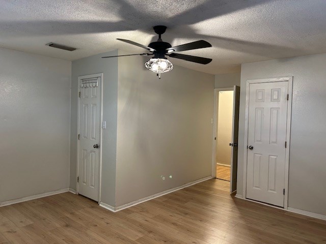 spare room featuring visible vents, a textured ceiling, baseboards, and wood finished floors