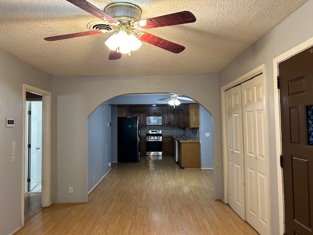 interior space featuring a textured ceiling, arched walkways, and light wood-type flooring