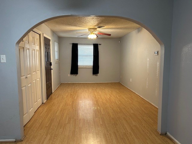 unfurnished bedroom featuring arched walkways, light wood finished floors, and a textured ceiling