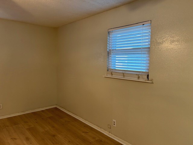 unfurnished room with a textured ceiling, baseboards, and wood finished floors