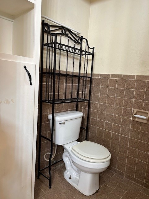 bathroom with a wainscoted wall, toilet, tile walls, and tile patterned flooring