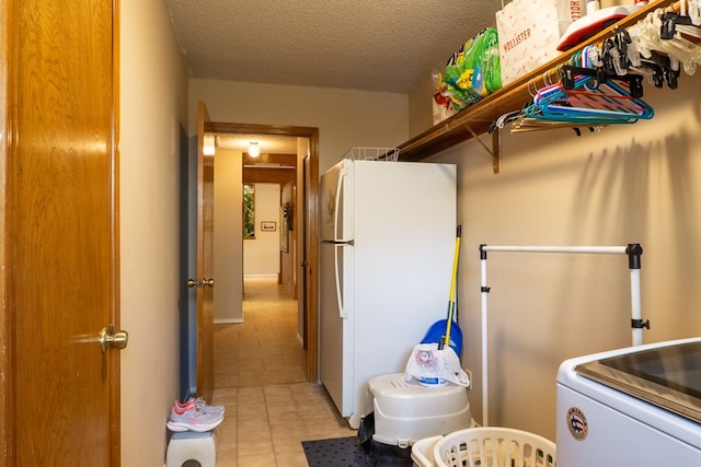 clothes washing area featuring a textured ceiling, laundry area, light tile patterned flooring, and washer / clothes dryer